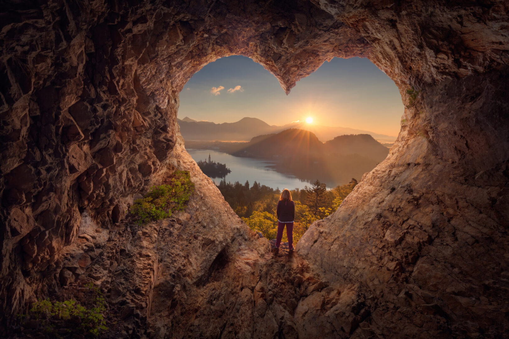 Lone woman enjoying in beautiful mountain nature, celebrating freedom and standing on edge of the cliff against the rising sun. Valentines day concept.