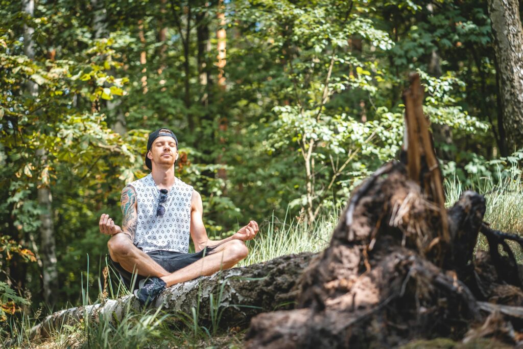 Man meditating on a log in forest.