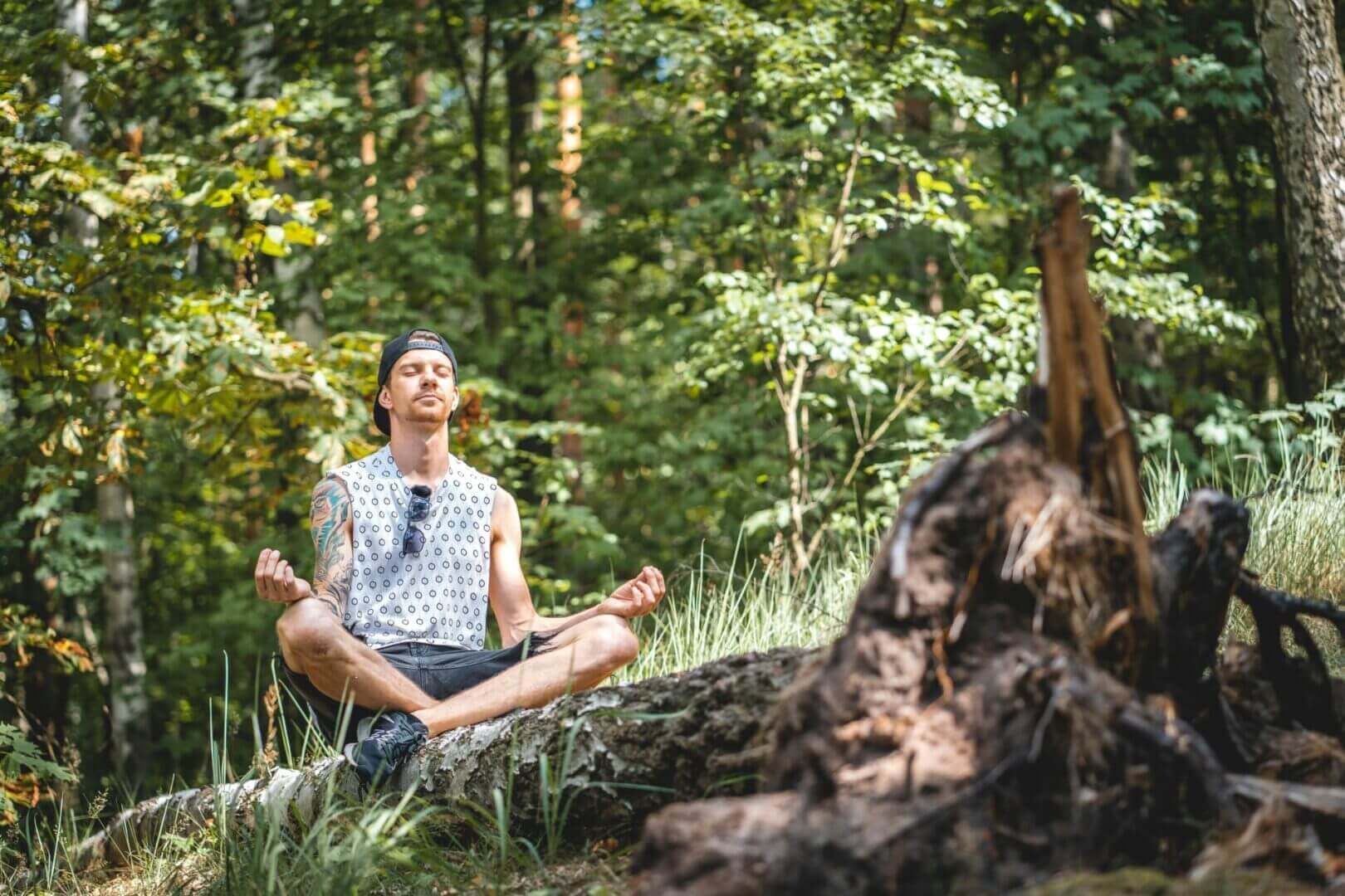 Man meditating on a log in forest.