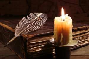 Candle, feather, and old book on table.