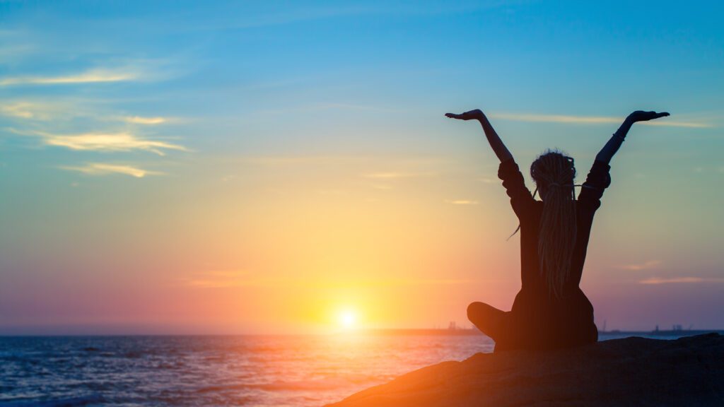 Person meditating by the ocean at sunset.